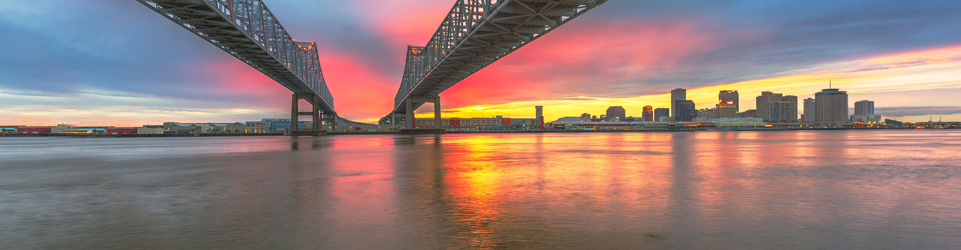 Sunset over the Mississippi and the New Orleans skyline beneath twin bridges
