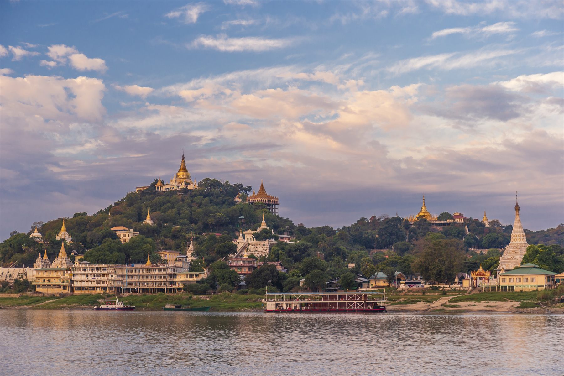 Golden pagodas on a wooded hillside above a wide river in Myanmar