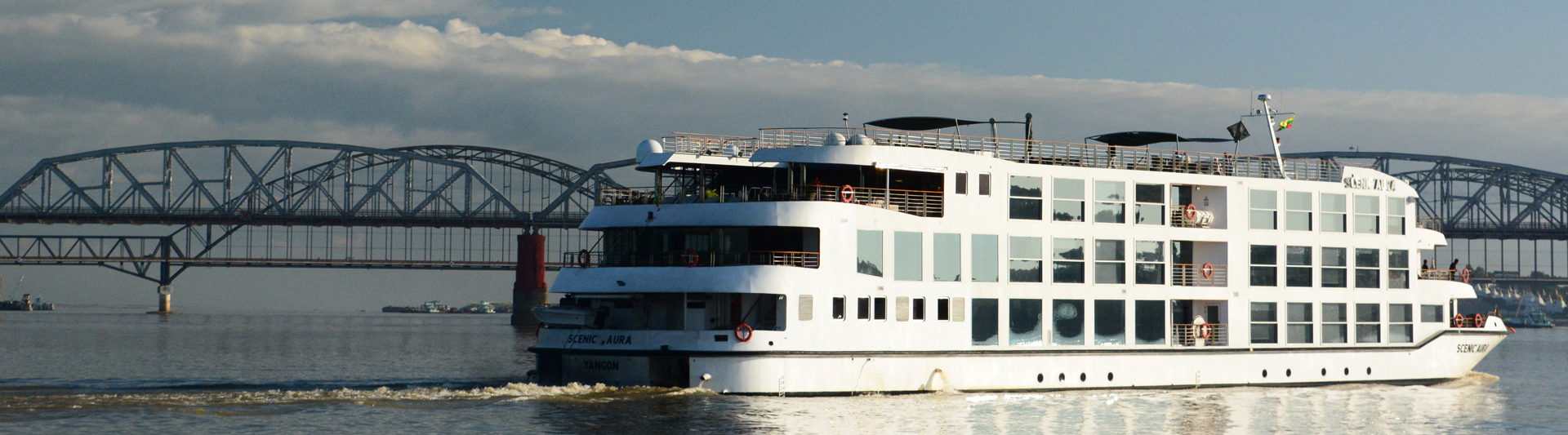 Three-deck river cruise ship passing a steel truss bridge